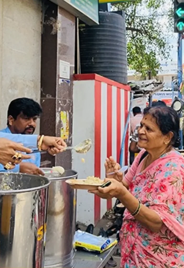 Dr. Chetan Kumar Mehta serving an Anna Danam meal to an elderly woman at a street feeding stop, Bengaluru