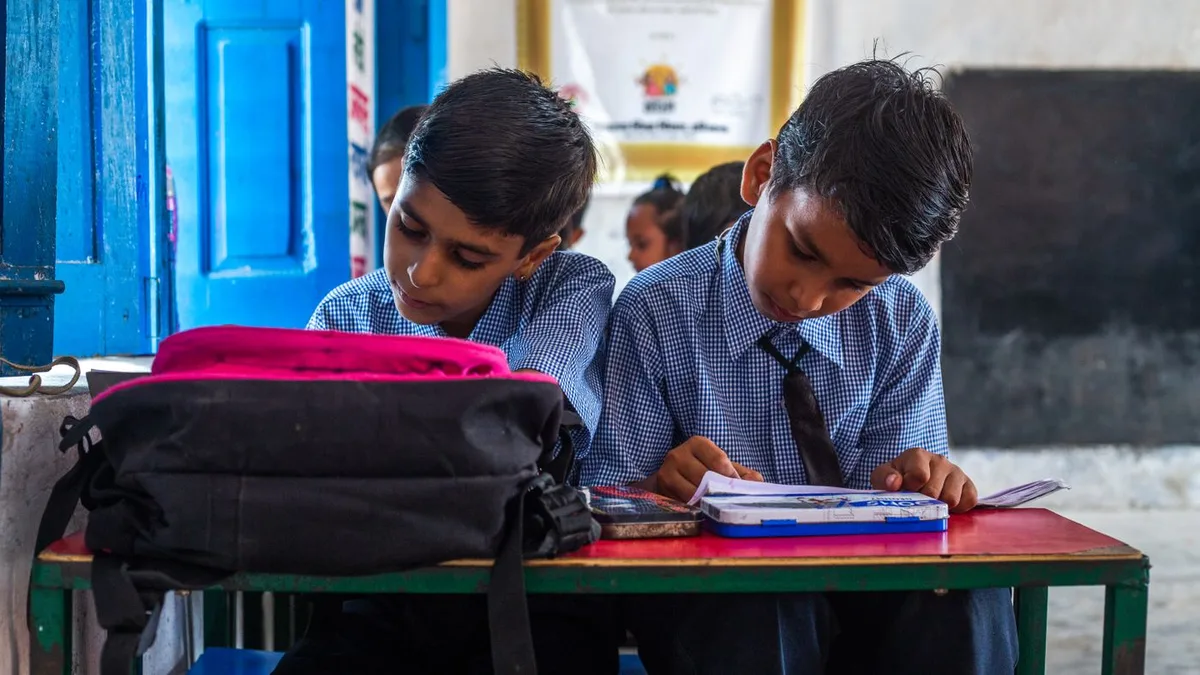 Two schoolboys in uniform studying together at a classroom desk with books and school bags